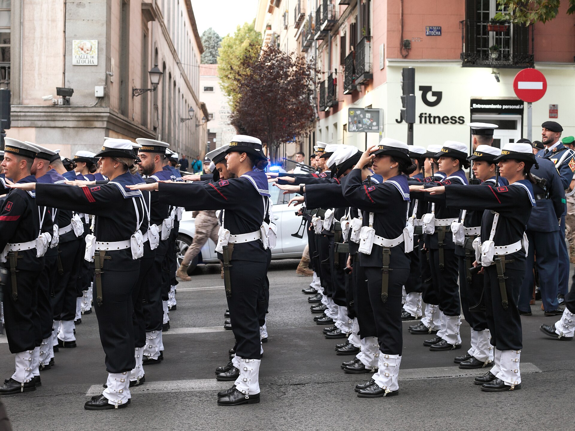 Una formación de marinos uniformados extiende el brazo en señal de saludo.