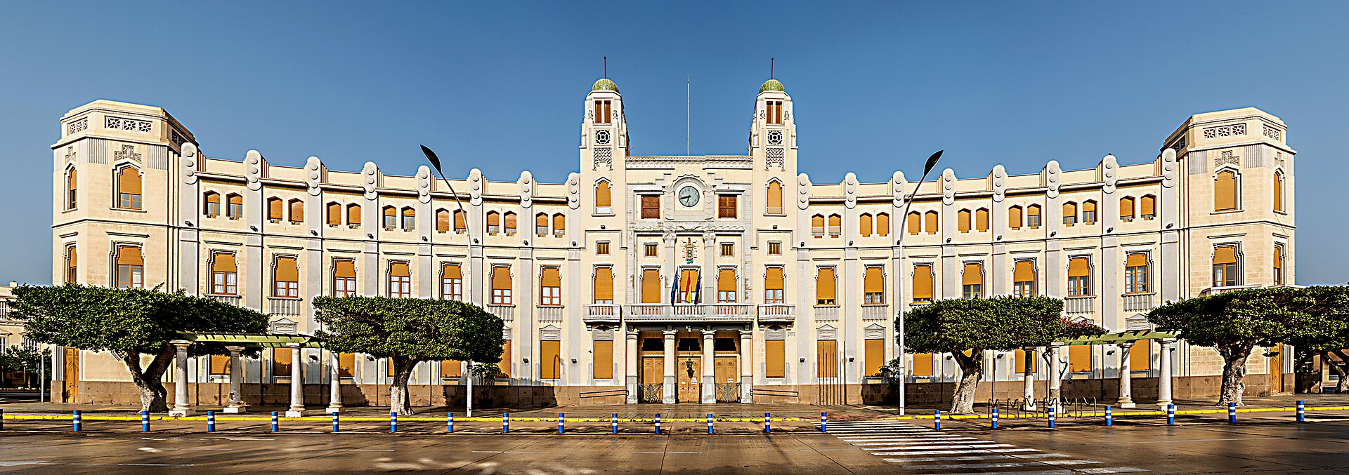 Fachada simétrica de un edificio institucional, con dos torres y un reloj sobre la entrada.