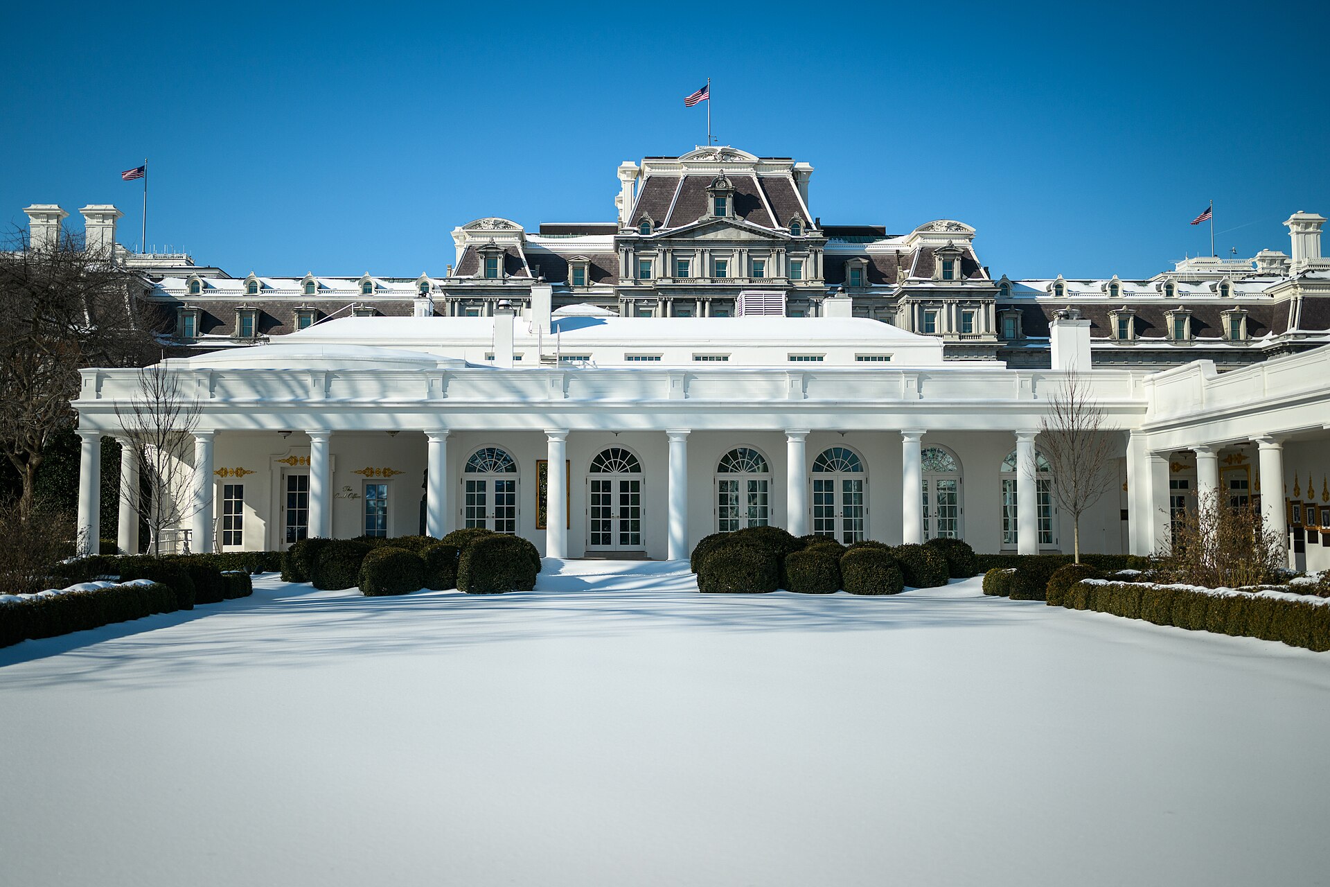 La fachada de un edificio oficial, con banderas estadounidenses y nieve en el jardín.