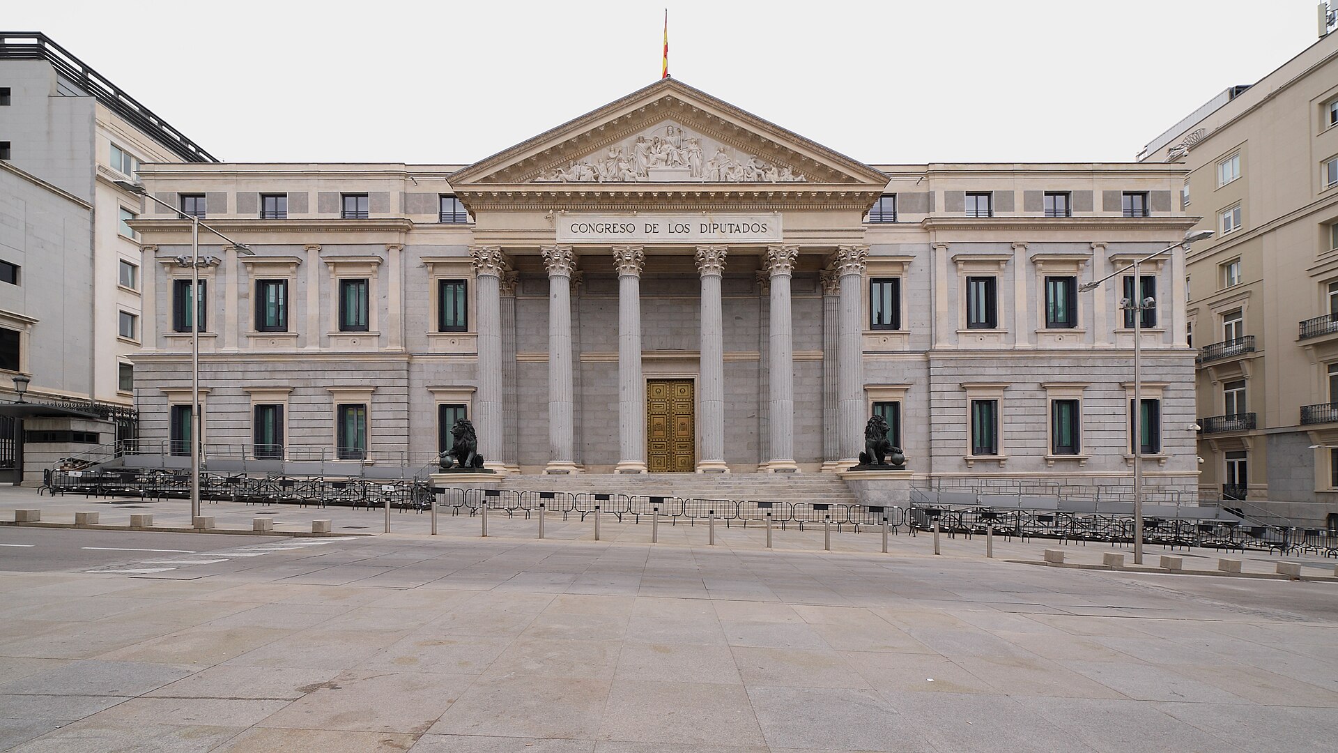 Vista amplia de un edificio con columnas y el rótulo «Congreso de los Diputados», rodeado de vallas.