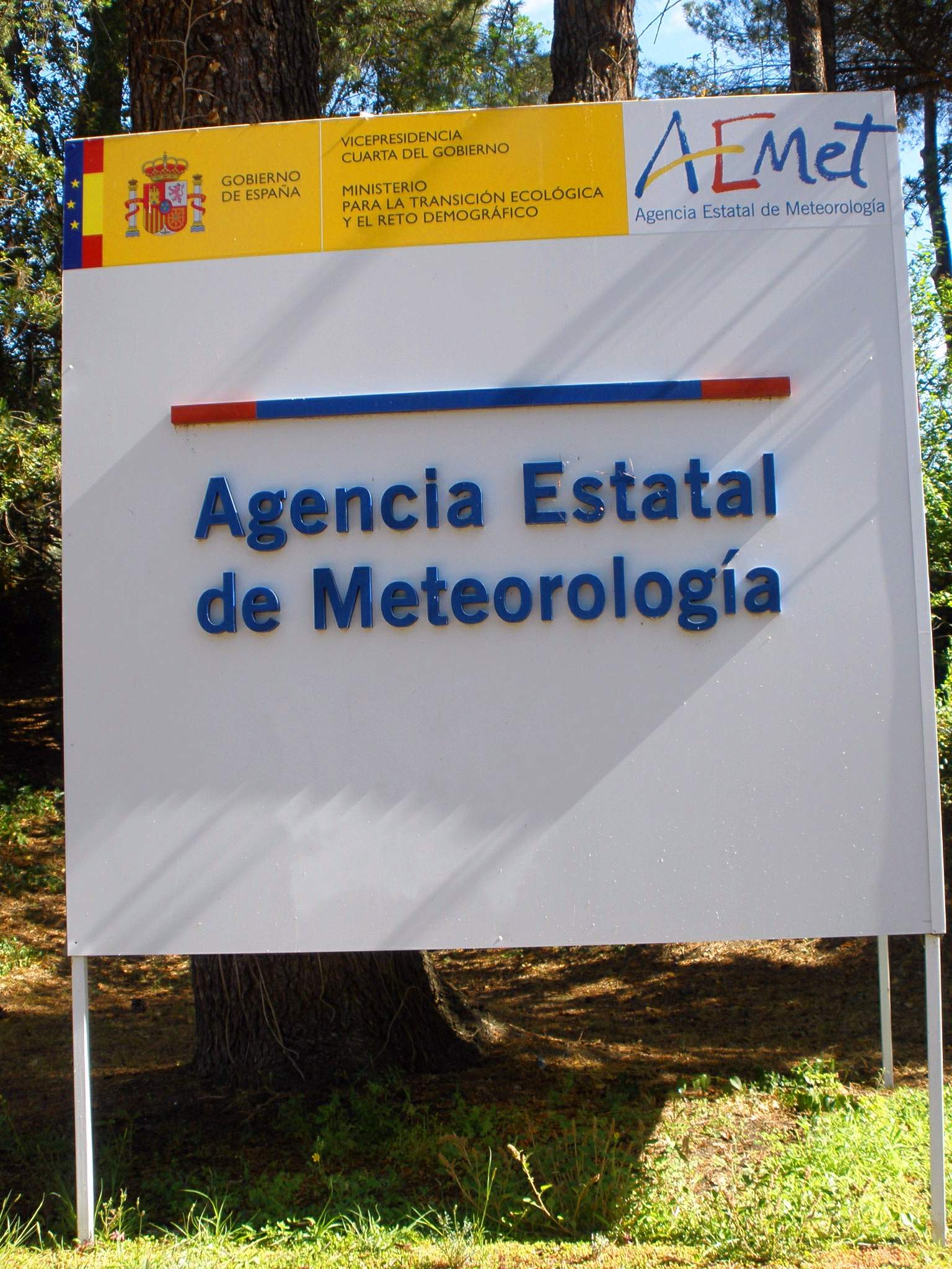 Un cartel con el nombre y el logotipo de la Agencia Estatal de Meteorología, rodeado de árboles.