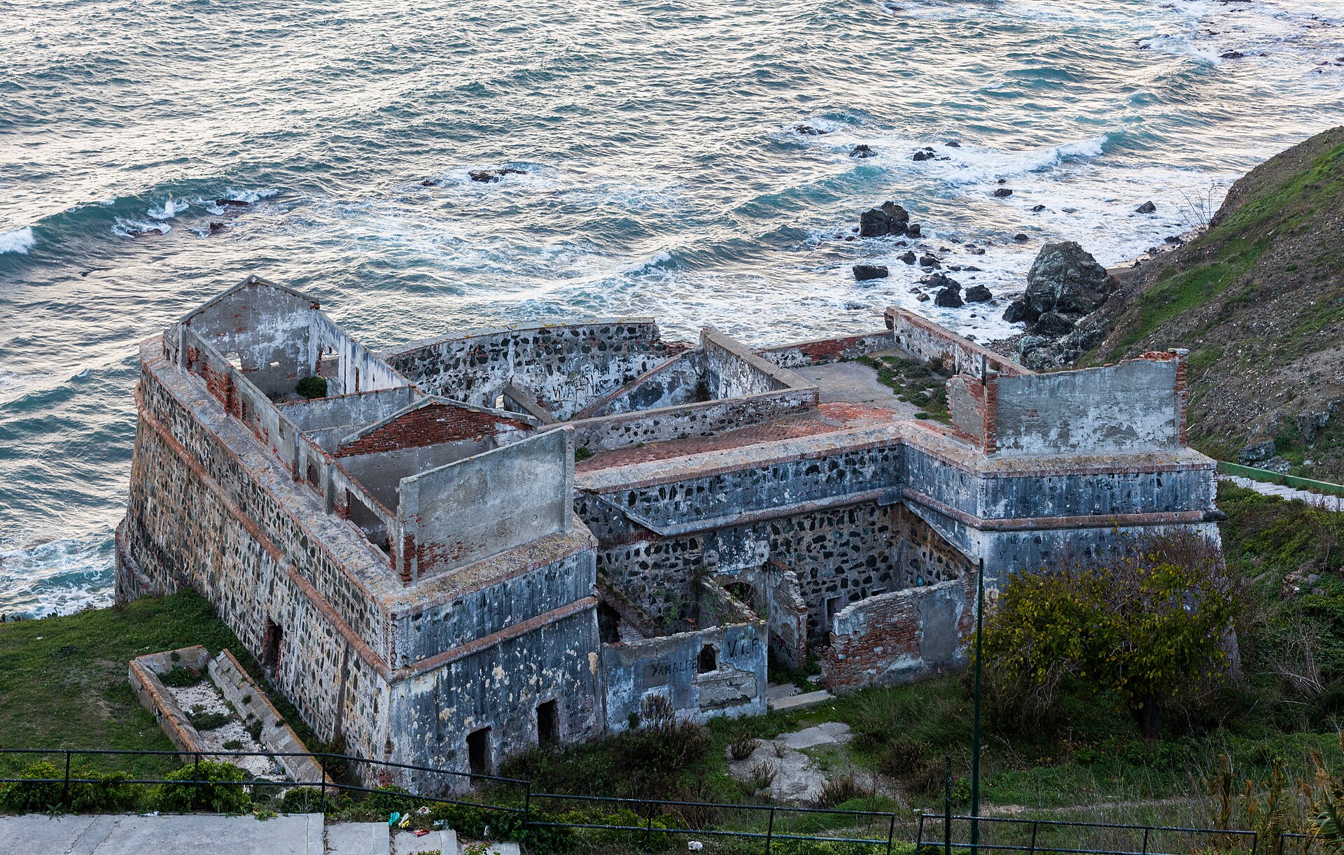 Ruinas de una construcción de piedra junto a la costa, con muros y estancias a cielo abierto.