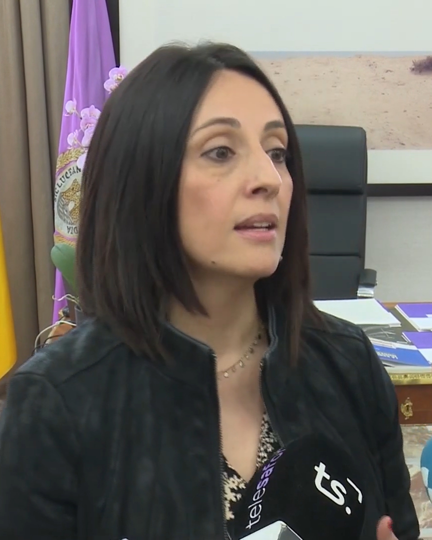 Una mujer, en primer plano, junto a un micrófono durante una entrevista en una oficina.