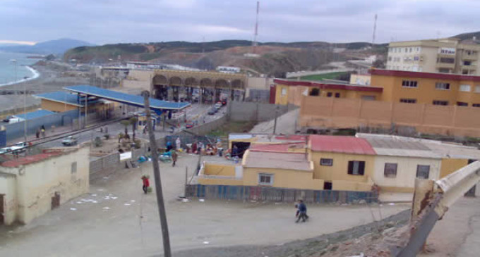 Vista elevada de una zona urbana junto a la costa, con edificios bajos, una vía transitada y varias personas en la calle.
