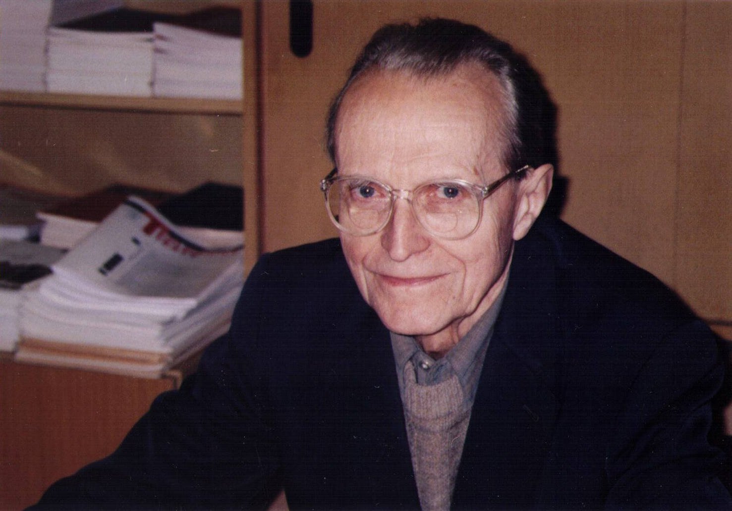 Retrato de un hombre con gafas sentado ante unos papeles.