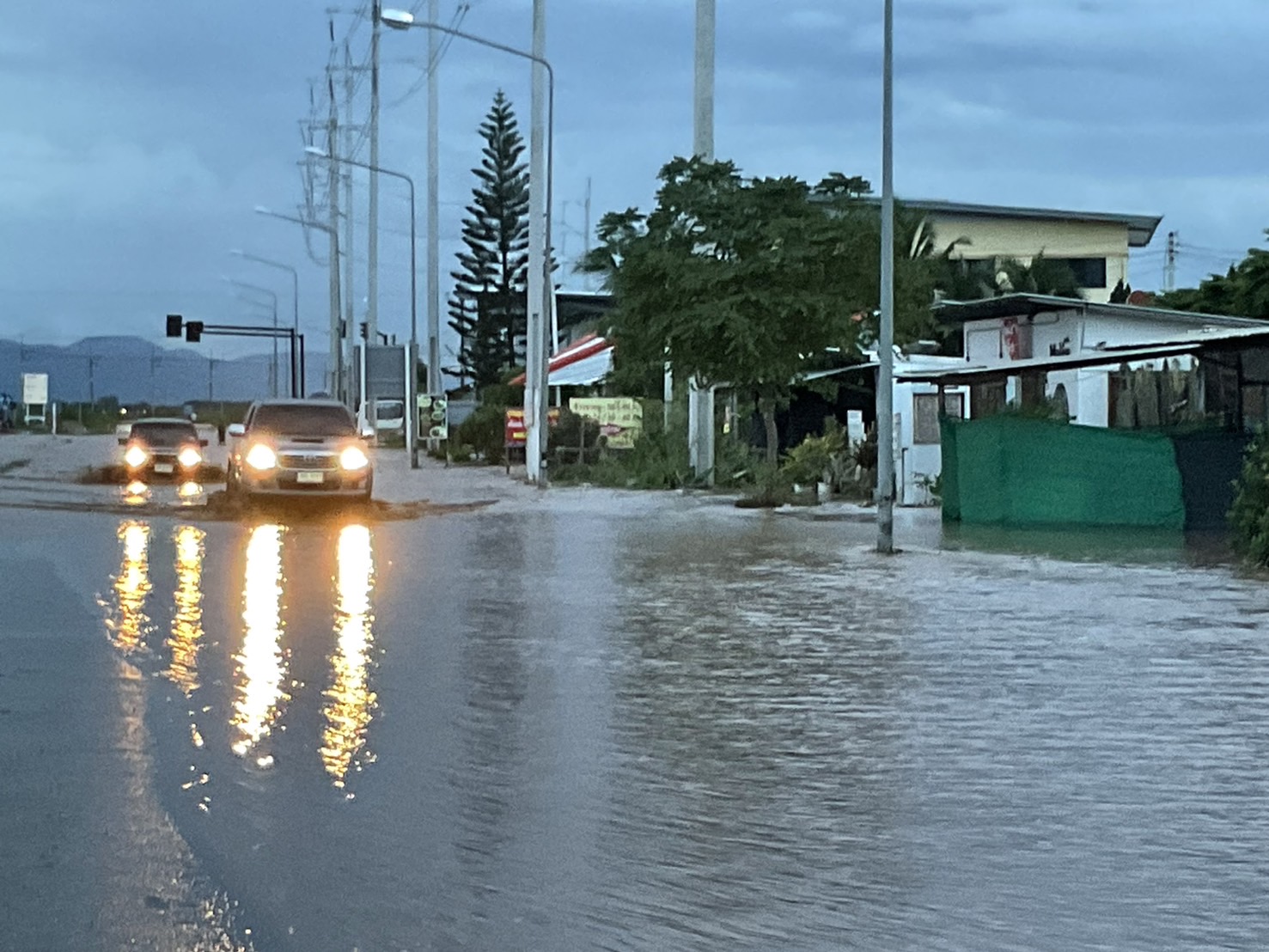Varios vehículos avanzan con los faros encendidos por una calle cubierta de agua.